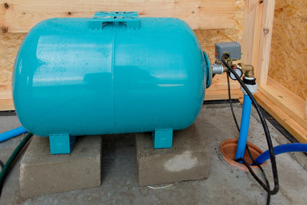 Teal horizontal well pressure tank on concrete blocks with a pressure switch at its fitting
