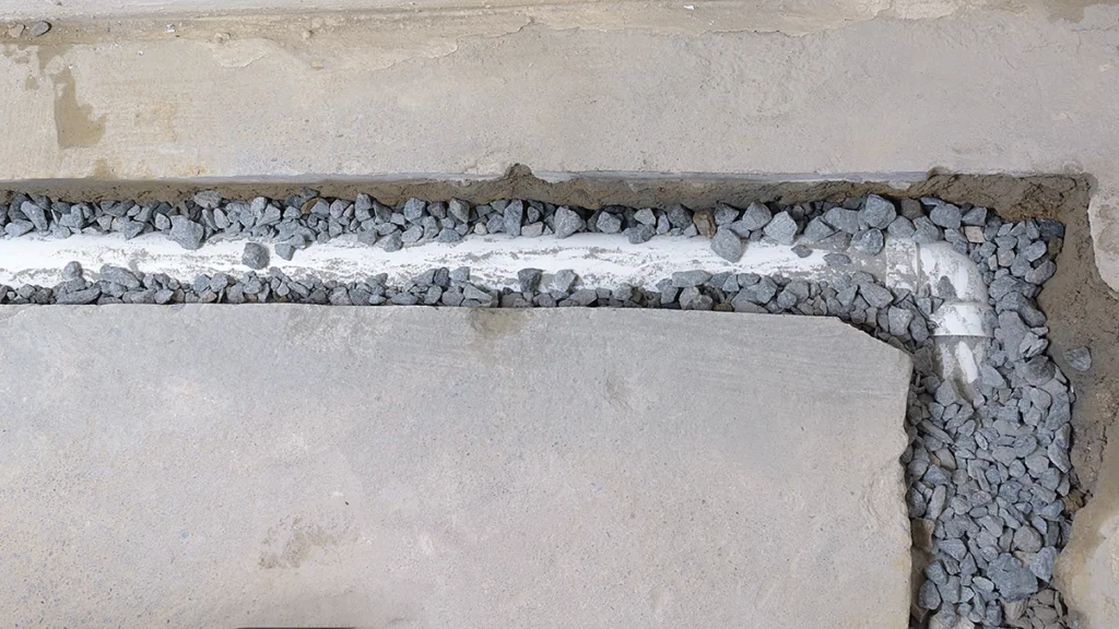 White perforated drain pipe laid in gravel along the base of a concrete foundation