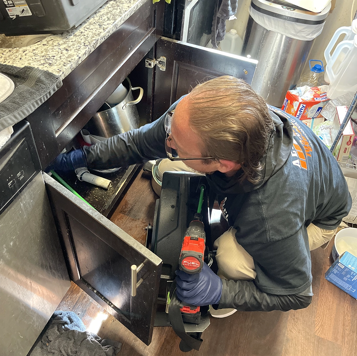 Technician performing kitchen drain cleaning under sink during service in Stafford VA