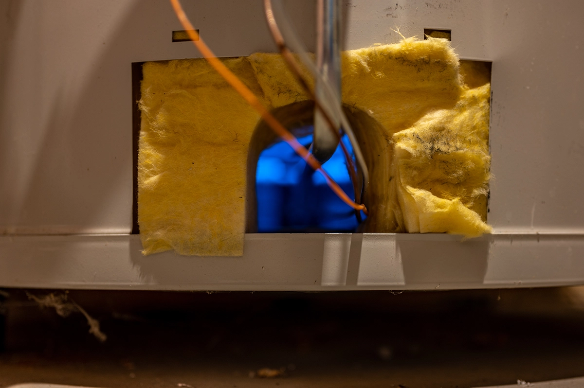 Water heater pilot light and burner assembly visible through access panel with blue flame