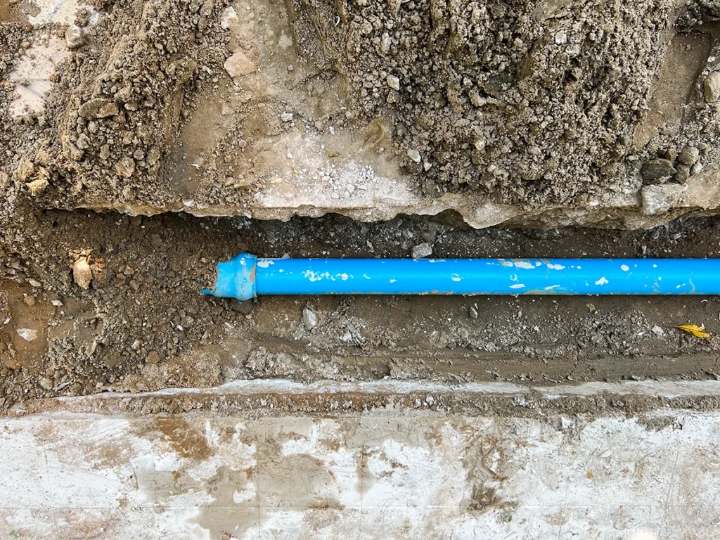 Underground residential water line made of blue PVC installed in a trench.
