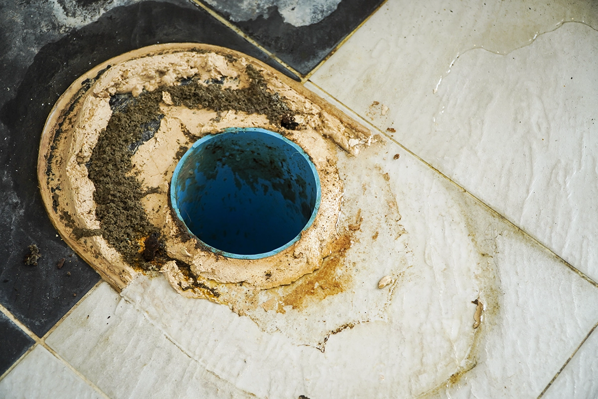 Close-up of a damaged toilet flange opening with old wax ring residue and floor staining, showing common offset toilet flange problems during toilet repair