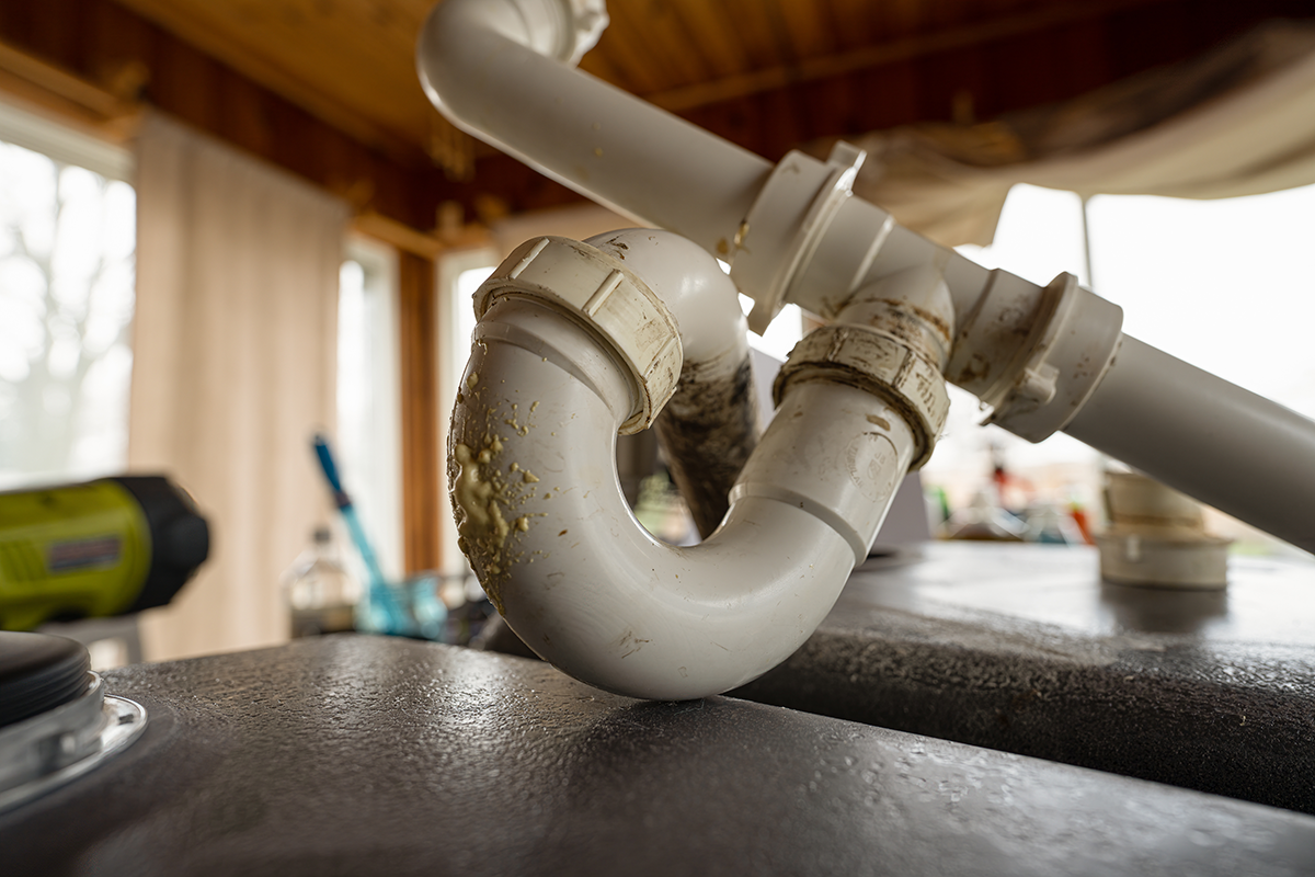 Close-up of a dirty p trap under a sink with visible buildup around the pipe connections